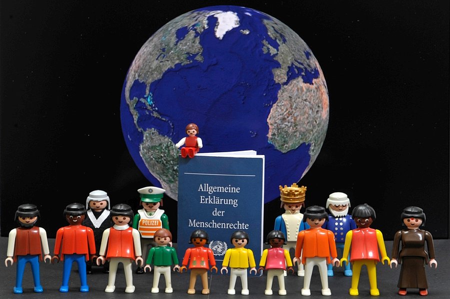 Viele verschiedene Playmobil-Figuren stehen vor einem Globus.