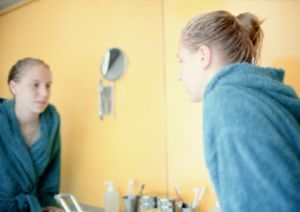 Ein Teenager schaut ihr Gesicht im Badezimmer-Spiegel an.